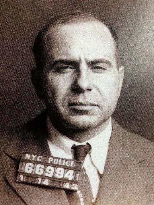 an old black and white photo of a man in a suit with a mug on his chest