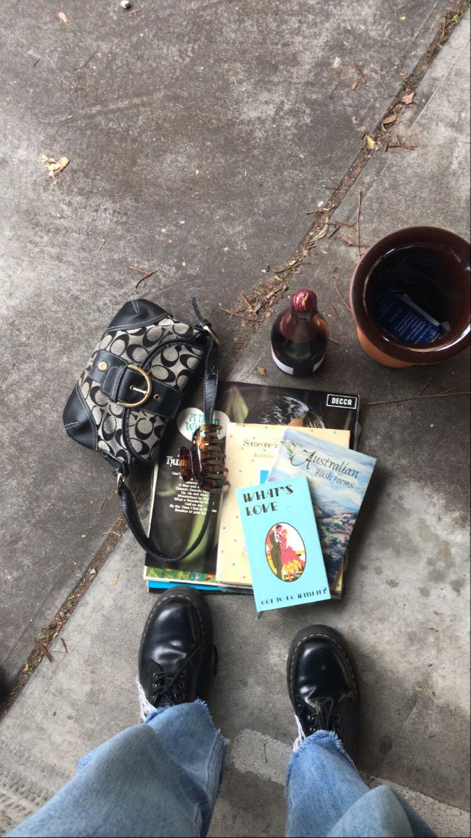 a person sitting on the ground with their feet up next to some books and a purse