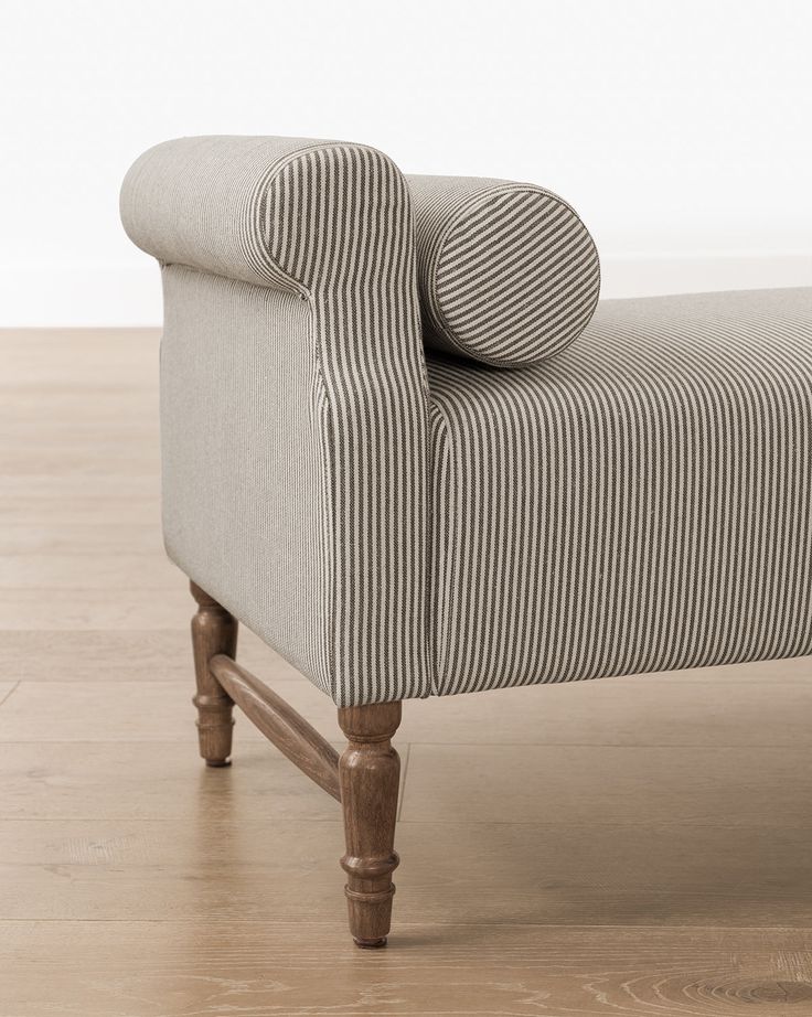 an upholstered bench with striped fabric on the armrests and wooden legs