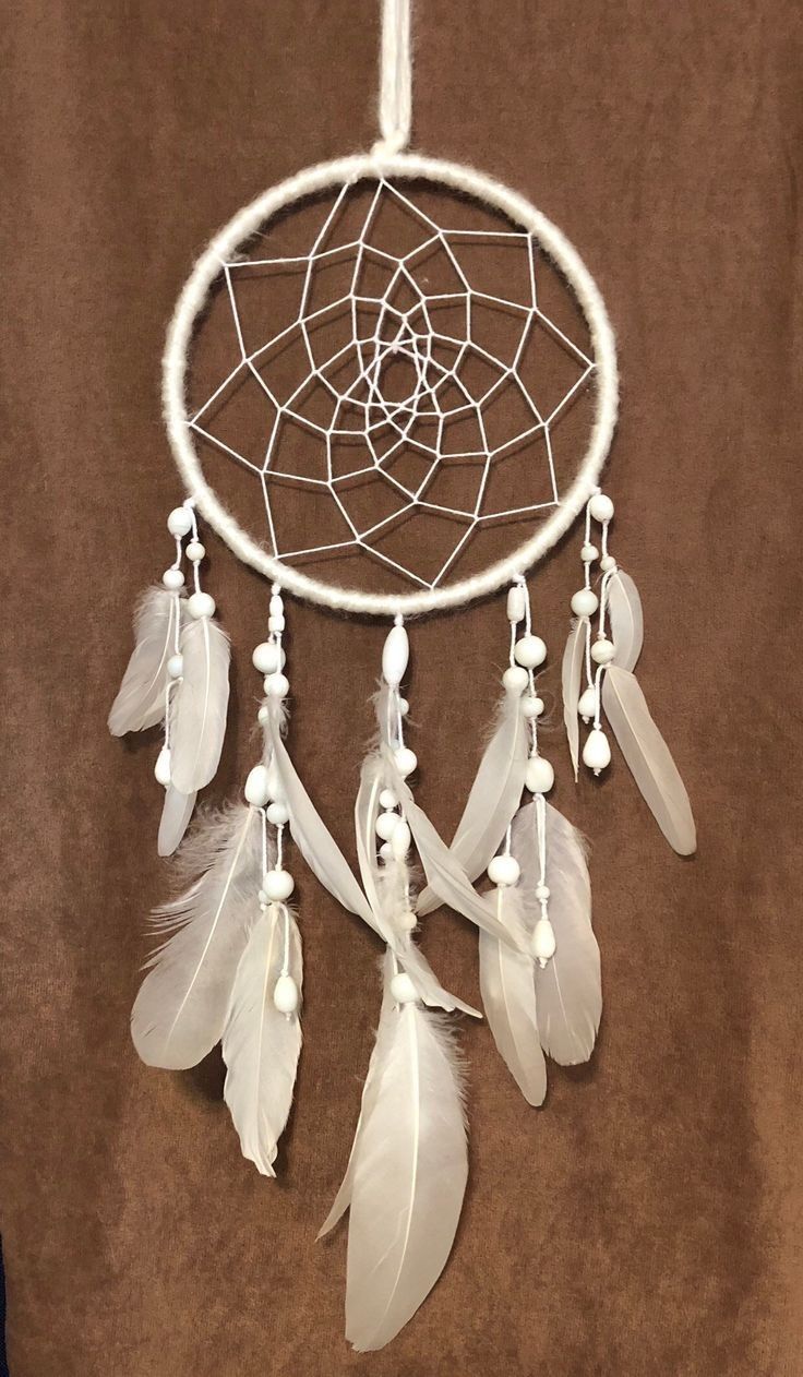 a white dream catcher with feathers hanging from it's side on a brown background