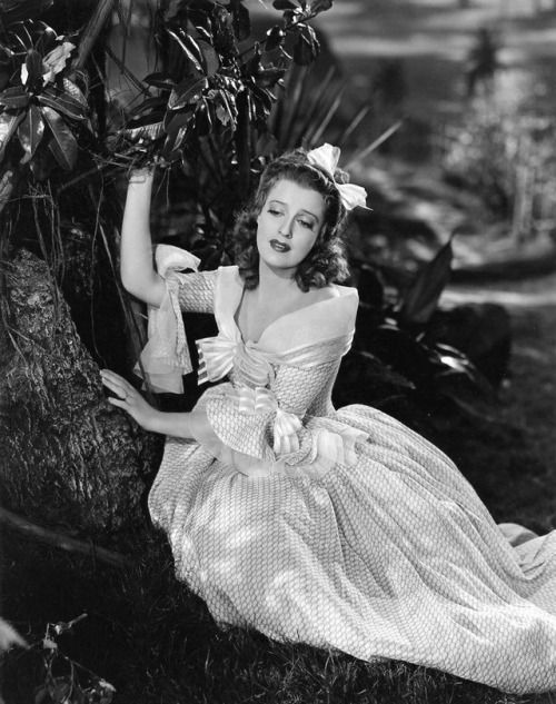 an old photo of a woman in a dress sitting on a tree branch with flowers