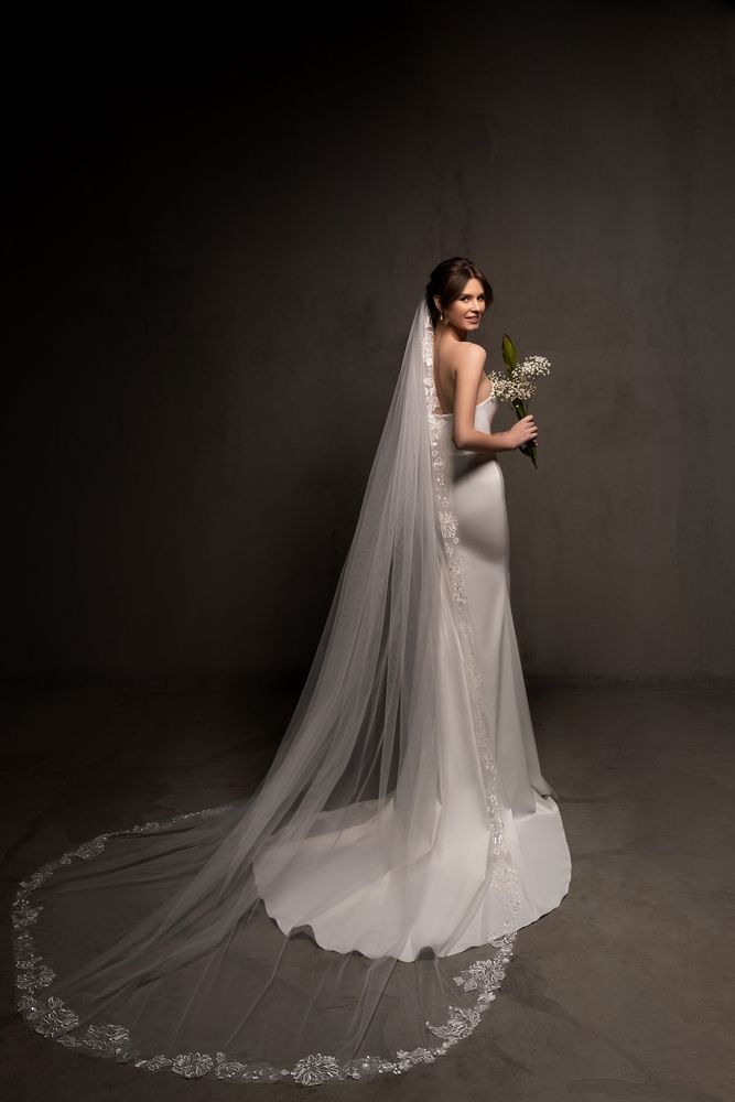 a woman in a wedding dress holding a flower and posing for the camera with her veil over her face