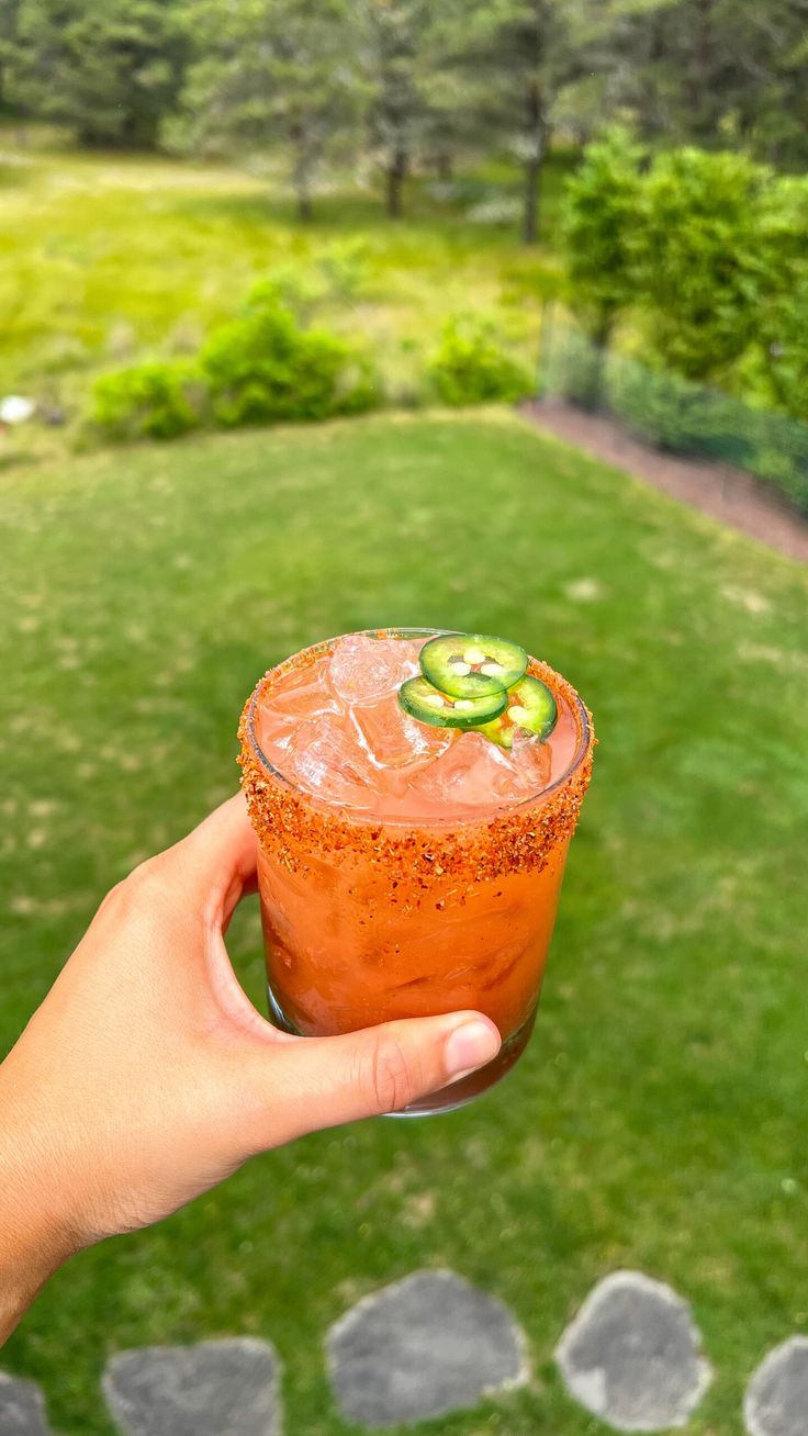 a person holding up a drink in their hand on top of a grass covered field