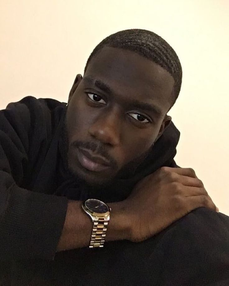 a man with his arms crossed wearing a black shirt and gold watch on his wrist