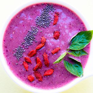 a white bowl filled with purple liquid and topped with green leafy garnish