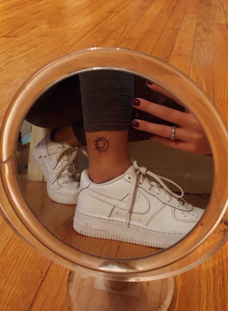 a woman's foot with a tattoo on her left ankle, reflected in a mirror