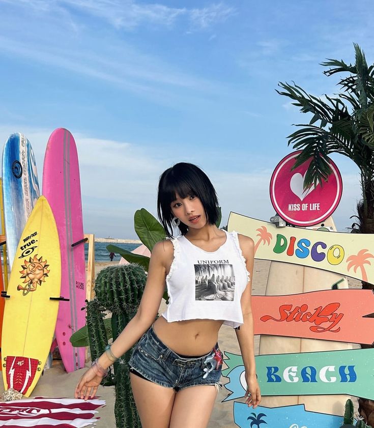 a woman standing in front of surfboards at the beach with her hand on her hip