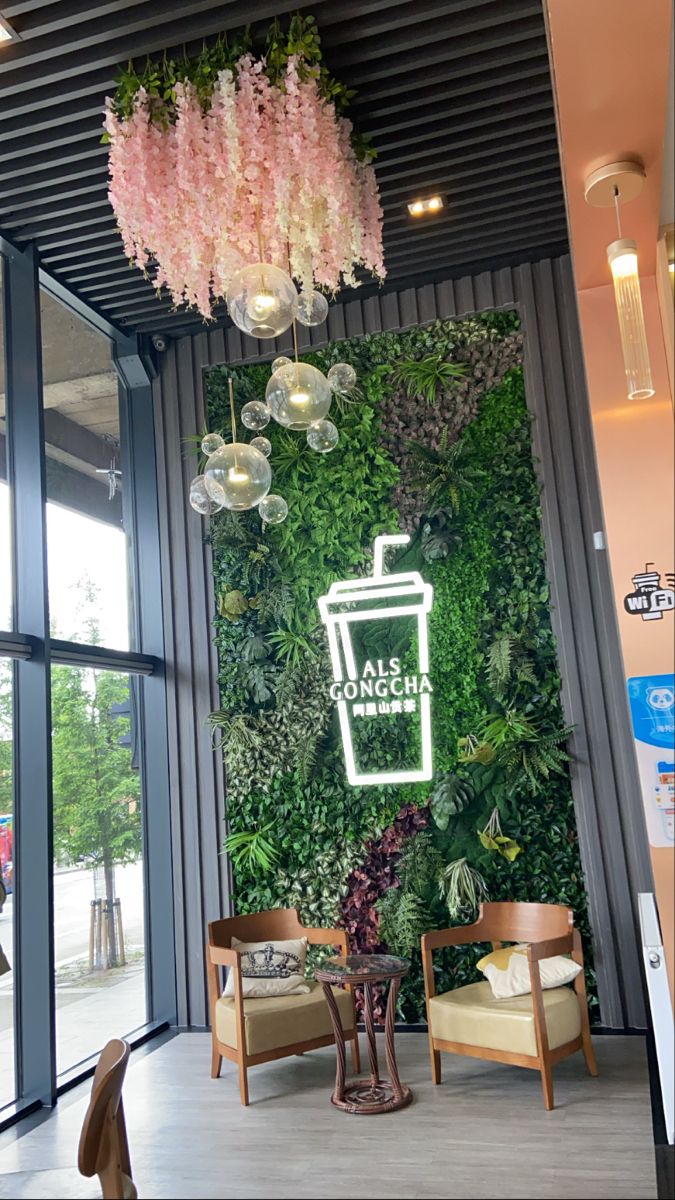 the inside of a coffee shop with pink flowers and greenery hanging from the ceiling