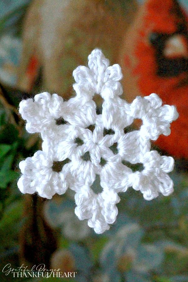 a crocheted snowflake is shown in front of a red and white christmas ornament