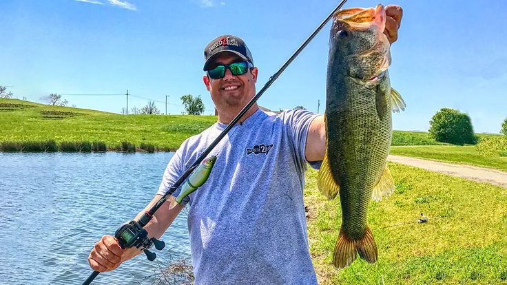 a man holding a fish while standing next to a body of water