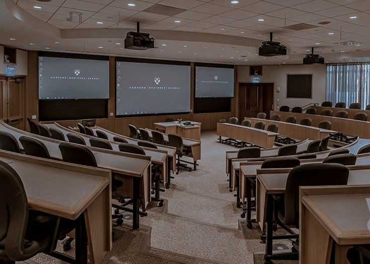 an empty room with tables and chairs in front of two large screen screens on the wall