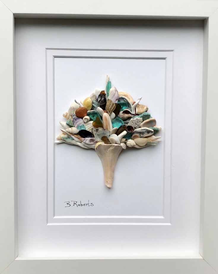 a white frame holding a painting with seashells and shells in the shape of a tree