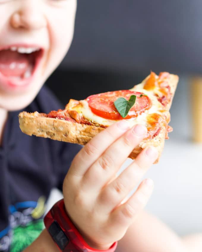 a young boy is eating a piece of pizza with tomatoes and basil on it's crust