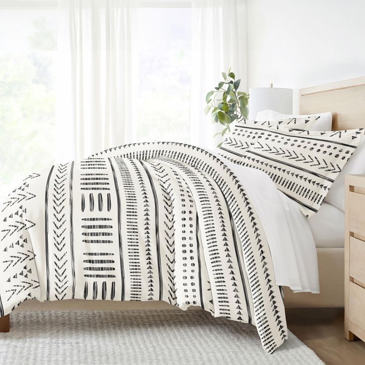 a white bed with black and white patterned comforter in a bedroom next to a window