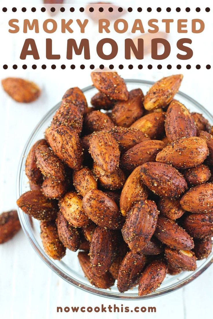 a glass bowl filled with roasted almonds on top of a white wooden table and text overlay reads smoky roasted almonds