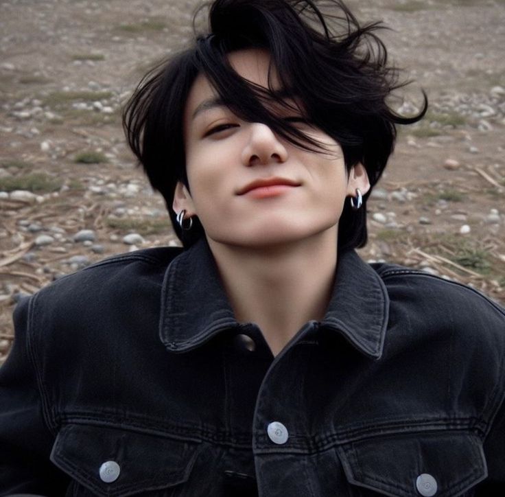 a woman with black hair and piercings sitting on the ground in front of rocks