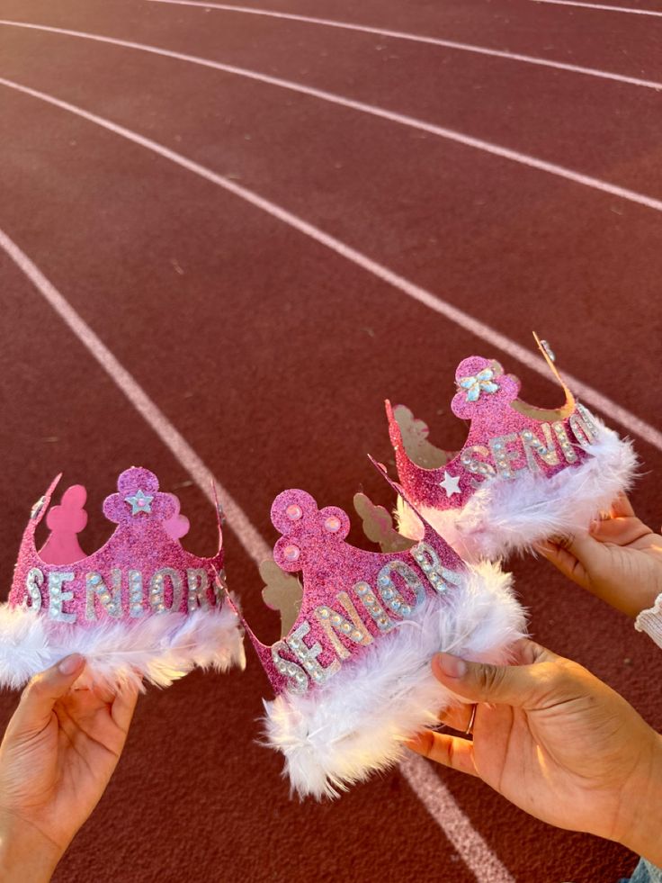 two people holding up pink and white tiaras on top of a race track,