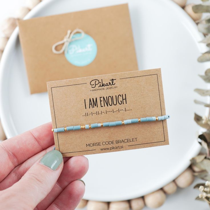 a person holding up a small beaded bracelet on top of a card with the words i am enough