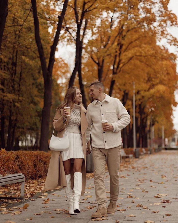 a man and woman walking down a sidewalk in the fall with leaves on the ground