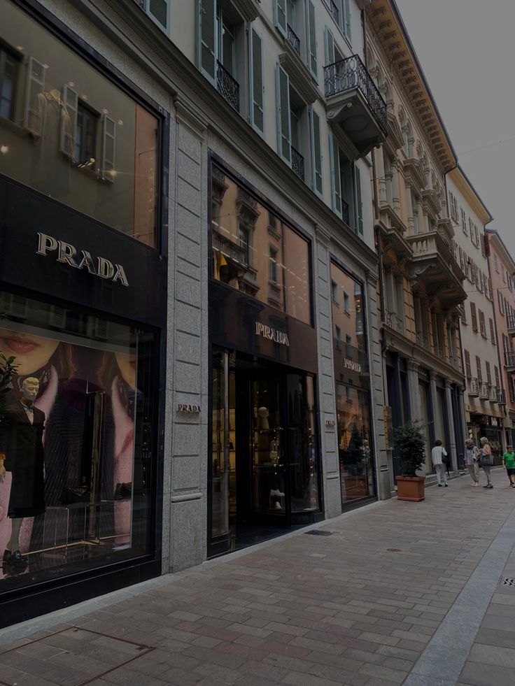 an empty sidewalk in front of a row of buildings with people walking on the sidewalk