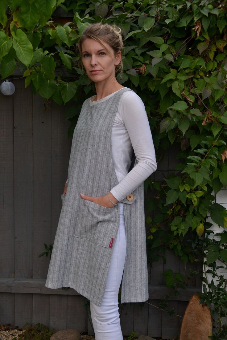 a woman standing in front of a fence wearing white pants and a gray top with pockets