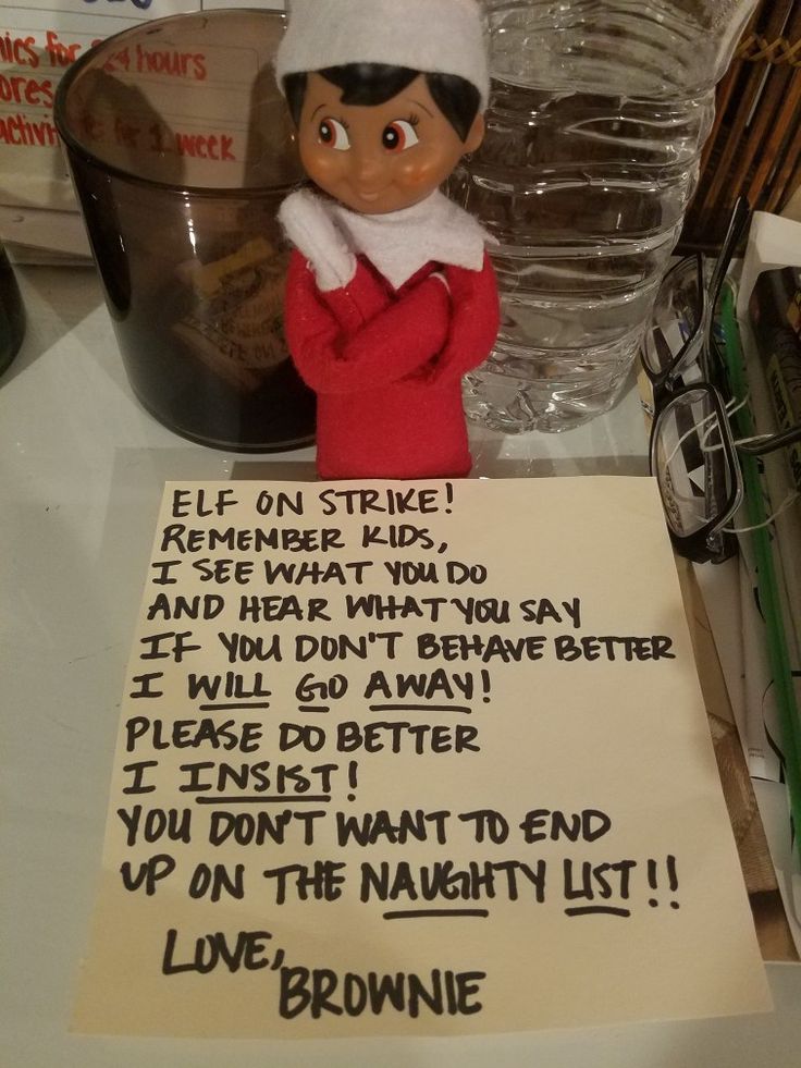 an elf is holding a sign on top of a table next to a glass bottle