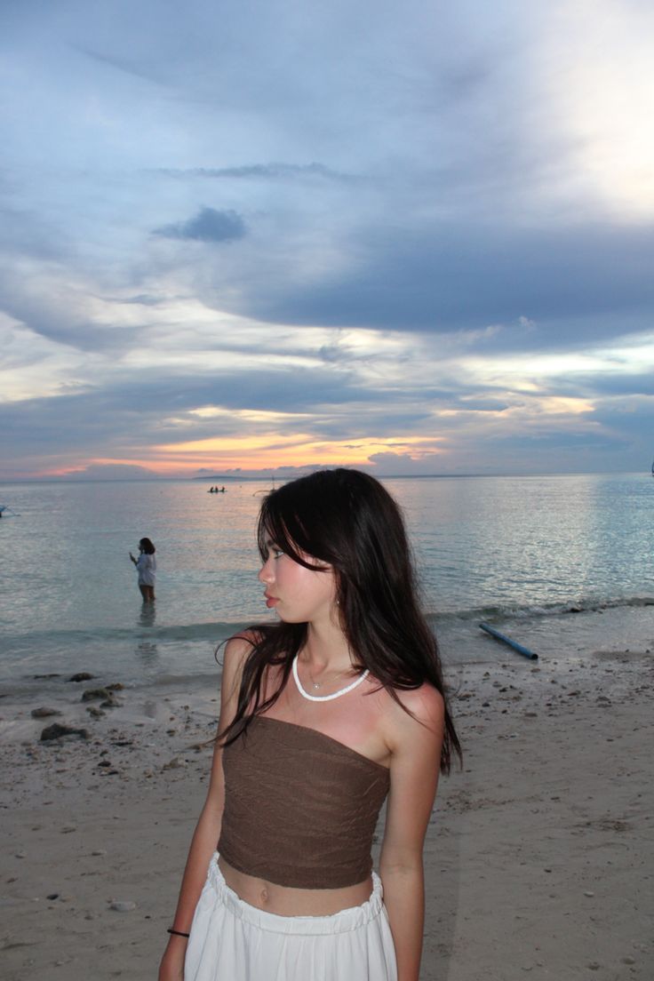 a young woman standing on top of a sandy beach next to the ocean at sunset