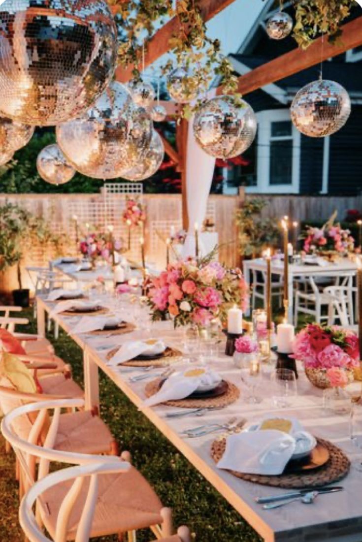 a long table set up for a party with pink flowers and disco balls hanging from the ceiling