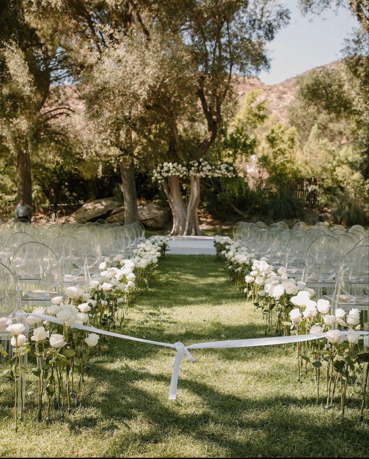 an outdoor ceremony setup with chairs and flowers on the grass, trees in the background