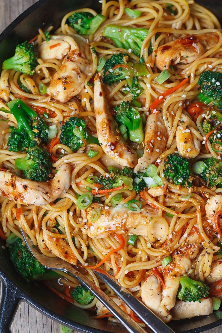 chicken and noodles with broccoli, carrots, and sesame seeds in a skillet