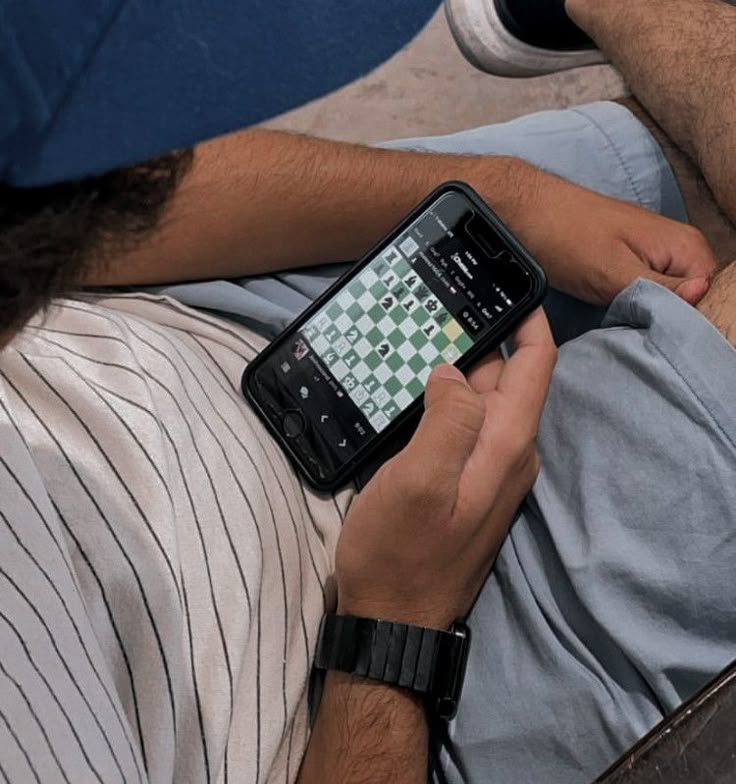 a man laying on the ground holding a cell phone in his hand while playing chess