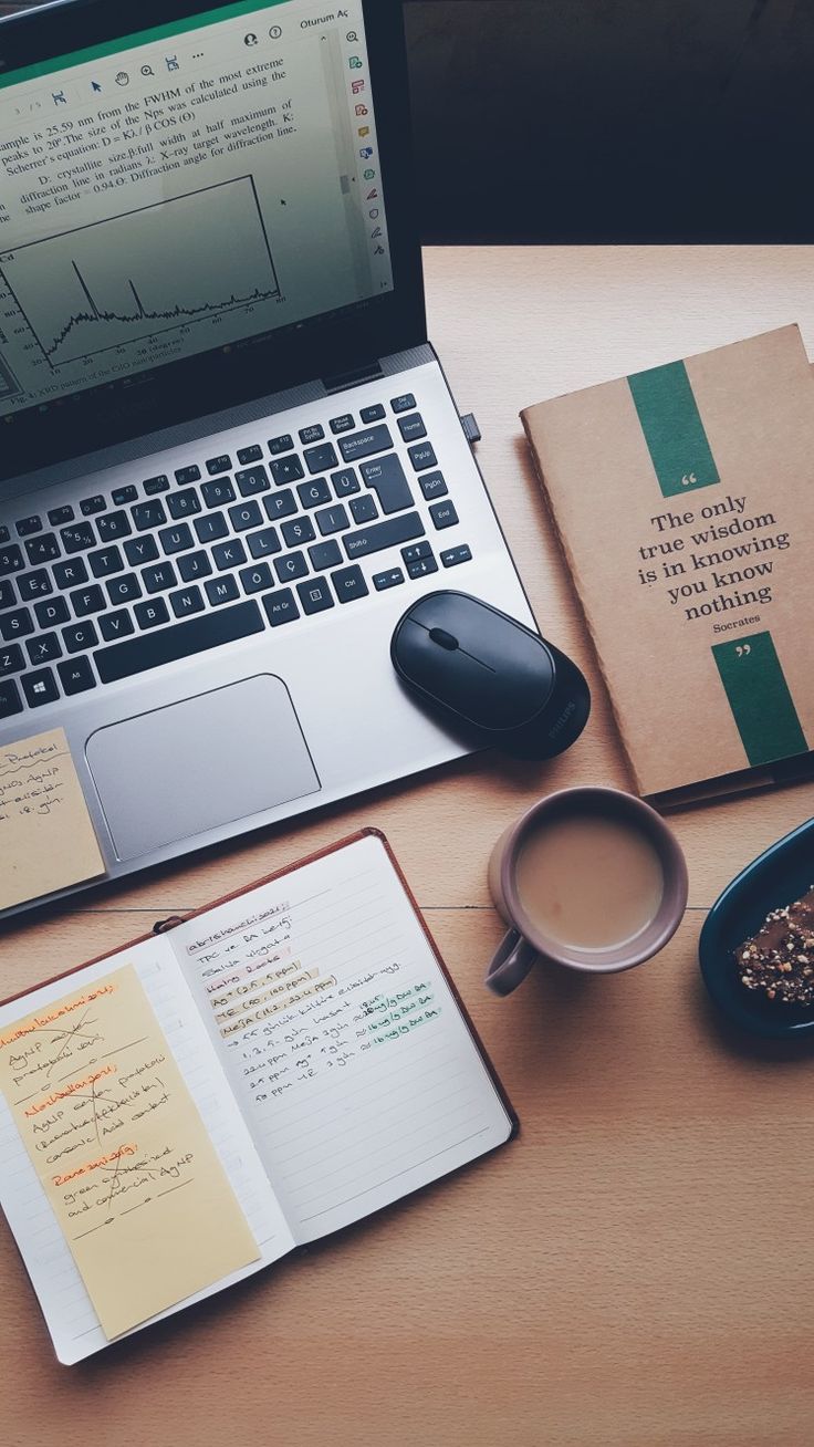 a laptop computer sitting on top of a wooden desk next to a cup of coffee