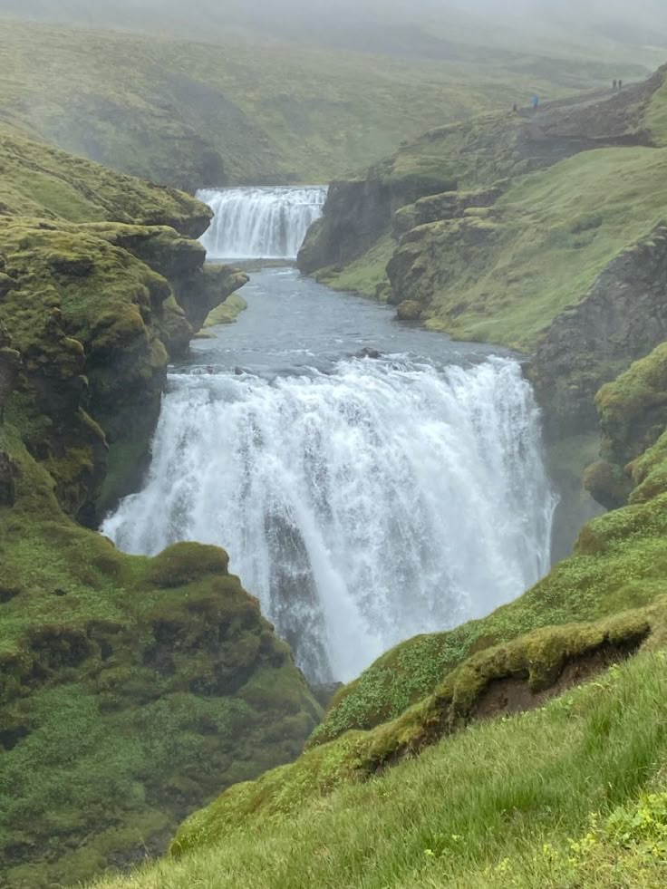 a large waterfall in the middle of a lush green valley