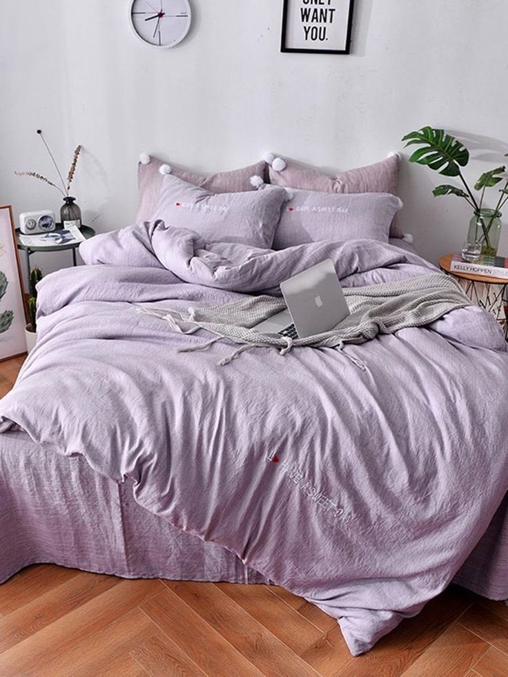 a laptop computer sitting on top of a purple comforter in a room with wooden floors