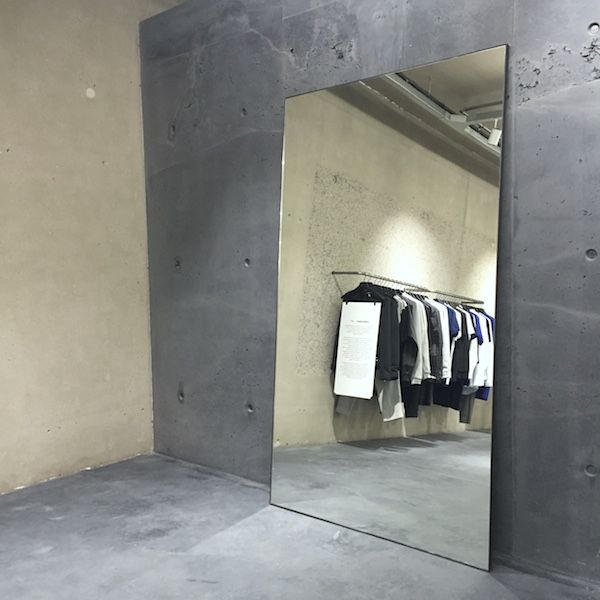 a mirror reflecting clothes in a room with concrete walls and flooring on the wall