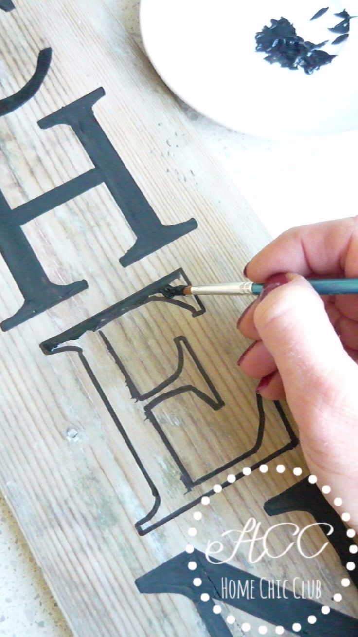 a person is painting the letters on a wooden board with black paint and pencils