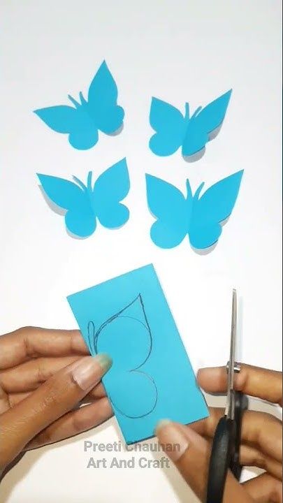 someone cutting out paper with scissors and some butterflies on the wall behind them in front of a piece of blue paper