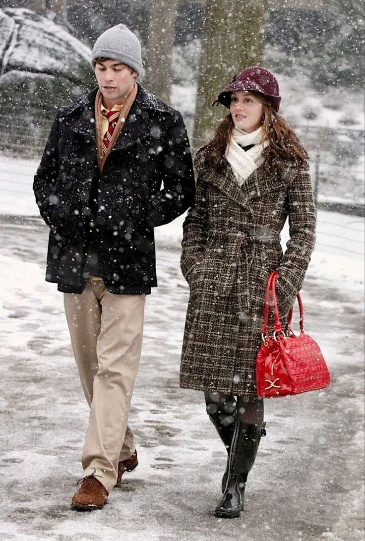 a man and woman are walking in the snow with one holding a red handbag