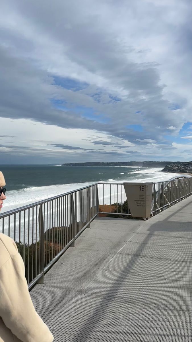 a man standing on top of a balcony next to the ocean and looking at the water