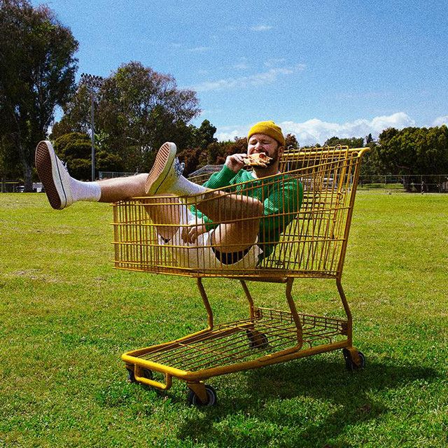 a man sitting in a shopping cart on the grass with his feet up and legs crossed