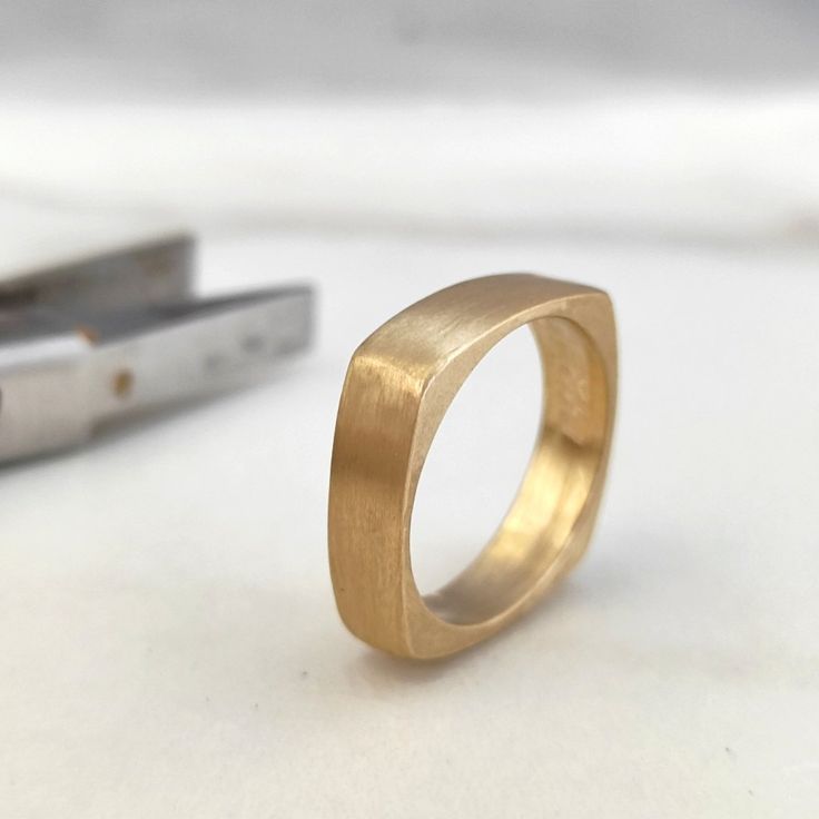 a gold ring sitting on top of a white table next to a pair of scissors