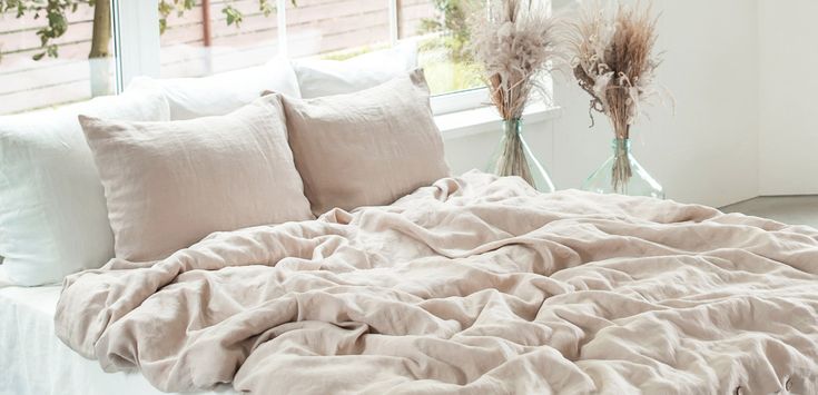 an unmade bed with two vases on the window sill next to it