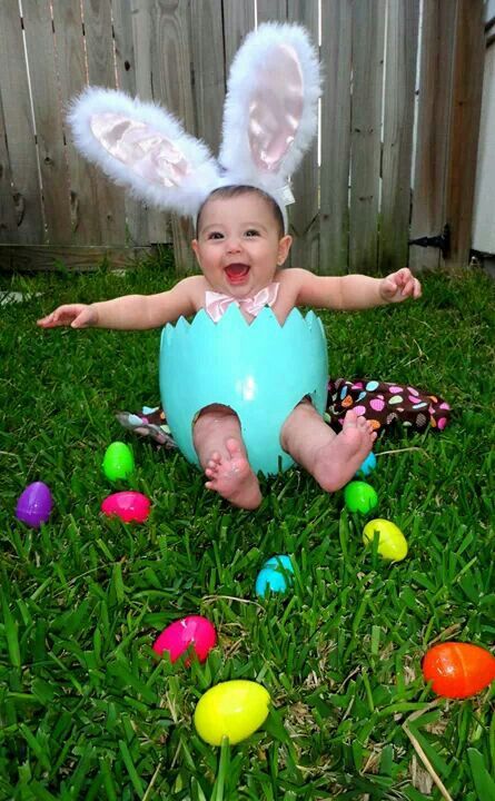 a baby sitting in the grass wearing an easter egg costume