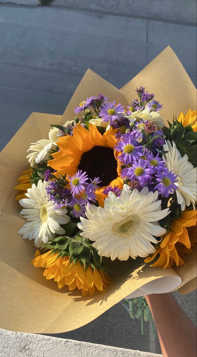 a bouquet of sunflowers, daisies and other flowers is held by someone's hand