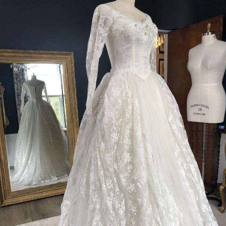 a white wedding dress on display in front of a mirror and mannequins