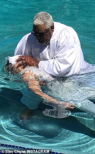 an older man swimming in the water with his arm around someone's leg while wearing sunglasses