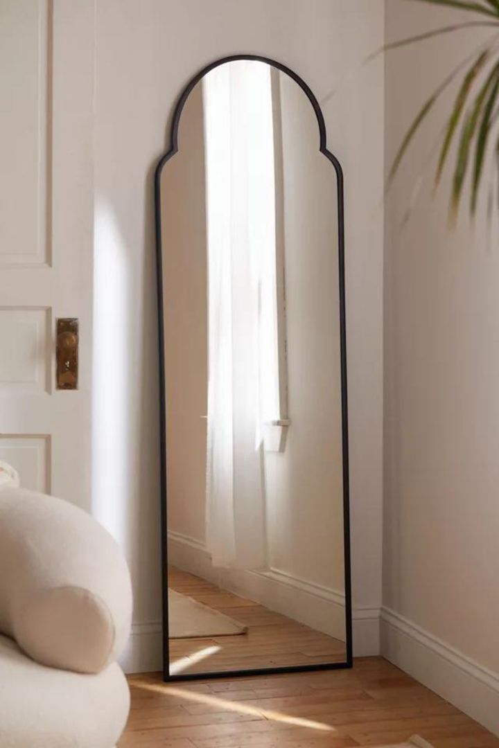 a large mirror sitting on top of a wooden floor next to a white chair and potted plant