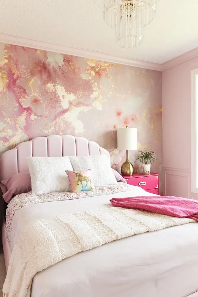 a pink and gold bedroom with white bedding, chandelier, pillows and lamps