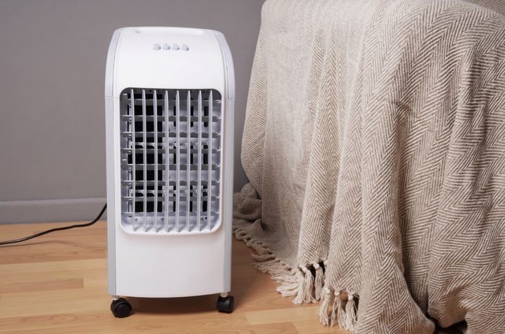 an air conditioner sitting on top of a wooden floor next to a blanket and pillow