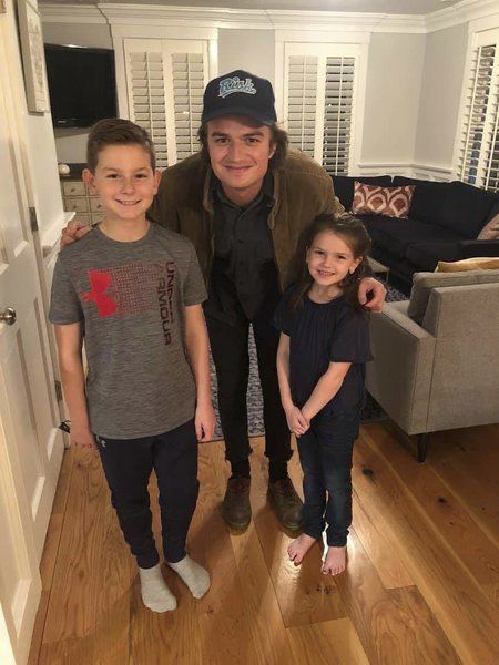 a man standing next to two children in a living room with wood floors and white walls